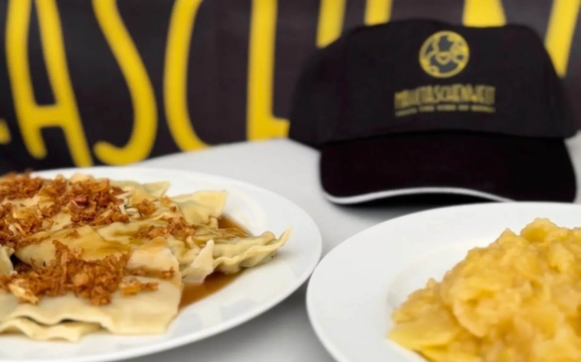 Frisch angerichtete Maultaschen mit Rostzwiebeln und Apfelmus vor dem Markenhintergrund der Maultaschenwelt.