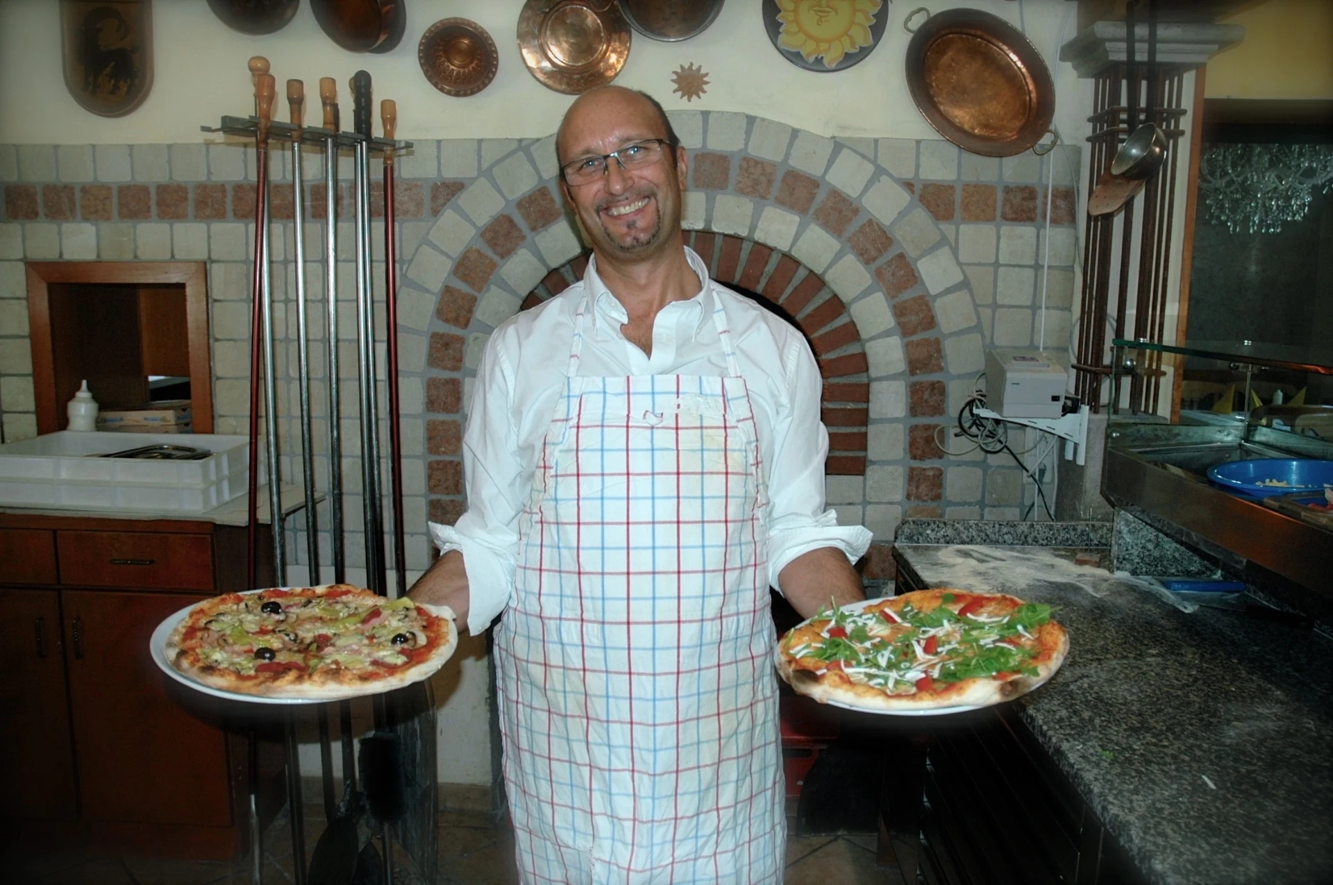 Pizzaiolo der Pizzeria zur Sonne mit zwei frischen Pizzen vor dem Steinofen.